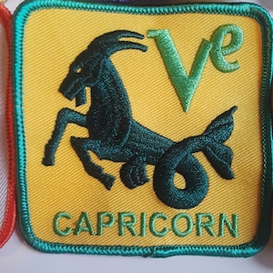 Op de afbeelding: Een gele viltpatch met een groene rand. De patch heeft een groene geborduurde letter "V" en een zwart-groene geborduurde afbeelding van een zeeboter. De tekst "CAPRICORN" is in groen onder de afbeelding geborduurd.