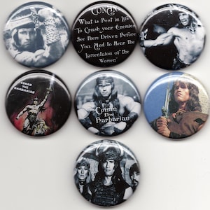 May include: Six round, silver-colored buttons with images of Conan the Barbarian. The buttons feature different scenes from the movie, including Conan holding a sword, Conan with a quote about crushing enemies, and Conan with a group of women. The buttons are all about 2 inches in diameter.