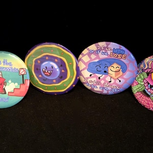 May include: Five colorful, round buttons with unique illustrations. Designs include a purple pattern, a scene with characters and text, a donut-like design, a brain with text, and a floral character. Each button is approximately 2 inches in diameter.