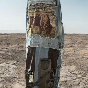 Könnte beinhalten: Ein langer Jeansmantel mit Patchwork-Design. Der obere Teil ist eine hellblaue Jeansjacke mit einer Landschafts- und Bison-Grafik auf dem Rücken. Der untere Teil ist ein Patchwork aus verschiedenen Jeans-Farbtönen mit Taschen und dekorativen Nähten.