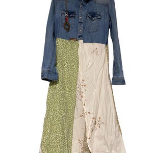 Może przedstawiać: Jeansowa sukienka typu patchwork z kołnierzykiem i długimi rękawami. Sukienka posiada panele z jasnoniebieskiego dżinsu, zielonej tkaniny w kwiaty i kremowej tkaniny z haftowanymi detalami. Wisiorek zwisa z dżinsu. Sukienka jest w unikalnym, boho stylu.