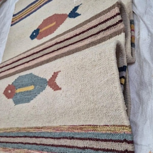 May include: Off-white woven rug with fish motifs. The rug features colorful fish designs in pink, blue, and yellow, along with striped borders in various colors. The text "ATAhomedecore" is visible.