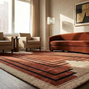 May include: A modern living room featuring a large, rectangular rug with a geometric design in shades of rust, black, and beige. The room includes a rust-colored sofa, two armchairs, and a floor lamp, creating a warm and inviting atmosphere.