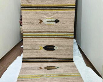 May include: A beige and brown woven runner rug with a fish pattern. The rug features horizontal stripes in brown, yellow, and black, and fish motifs in various colors. The rug is made of a textured material.