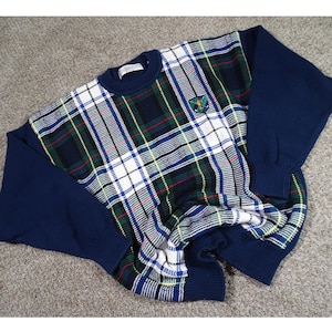 May include: A navy blue sweater with a plaid pattern in white, green, red, and navy blue. The sleeves and collar are solid navy blue. A small emblem is on the upper left chest.