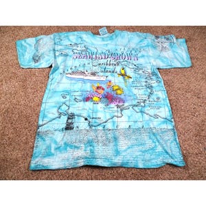 May include: A light blue t-shirt featuring a map of the Caribbean Islands with illustrations of a cruise ship, parrot, and coral reef. The shirt has the text "Seawind Crown Caribbean Islands" across the top.