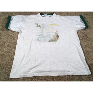May include: A light gray t-shirt with a green collar and sleeve cuffs. The shirt features a graphic of a lighthouse, a sailboat with a Union Jack sail, and a seagull. The text "Myrtle Beach" is above the lighthouse.