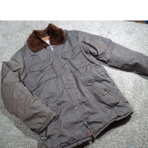 May include: A brown bomber jacket with a faux fur collar. The jacket has a zipper closure, multiple pockets, and a brown lining. The sleeves have a pocket with a zipper. The jacket is made of a durable material.
