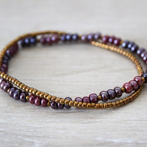 May include: A double-strand bracelet with small, dark red and gold beads. The bracelet is made of two strands of beads, one with dark red beads and the other with gold beads.
