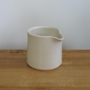 Jarra de crema pequeña y sencilla de cerámica, color blanco minimalista.