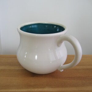 May include: White ceramic mug with a teal blue interior. The mug has a rounded body and a curved handle.