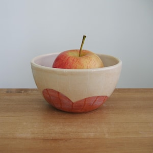 Puede incluir: Cuenco de cerámica color crema con un diseño rojo en forma de hoja en la base, que contiene una manzana roja y amarilla. El cuenco está sobre una superficie de madera. El diámetro del cuenco es de unos 15 cm.