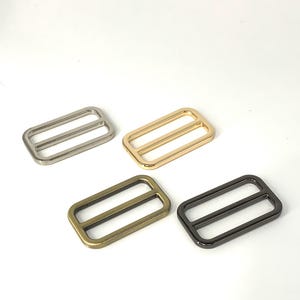 Puede incluir: Cuatro hebillas deslizantes de metal en diferentes acabados: plata, oro, latón antiguo y negro.