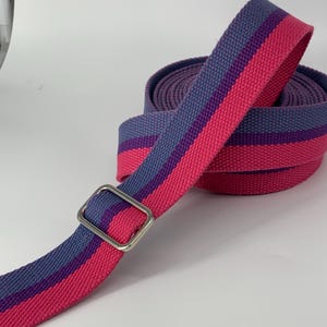 May include: A pink and purple striped fabric strap with a silver metal buckle. The strap is rolled up and ready to be used.