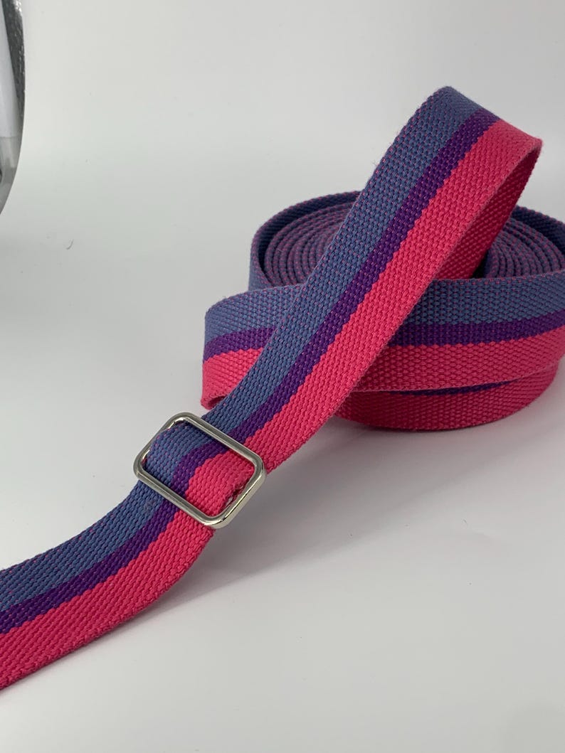 May include: A pink and purple striped fabric strap with a silver metal buckle. The strap is rolled up and ready to be used.