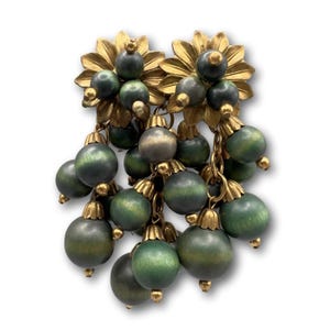 Può includere: Orecchini vintage con un motivo floreale dorato nella parte superiore e grappoli pendenti di perline di legno verdi. Le perline hanno un effetto sfumato, che va dal verde scuro al verde chiaro. Su sfondo bianco.