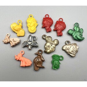 May include: A collection of colorful vintage Disney character charms, including Mickey Mouse, Donald Duck, and others. The charms are made of various materials and feature a loop for attaching to a necklace or bracelet. The charms are in various colors, including gold, red, and green.