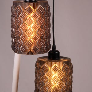 May include: Two pendant lights with a brown, textured glass shade. The shades have a diamond pattern and are lit from within, creating a warm glow. The lights hang from black cords and are attached to a white pole.