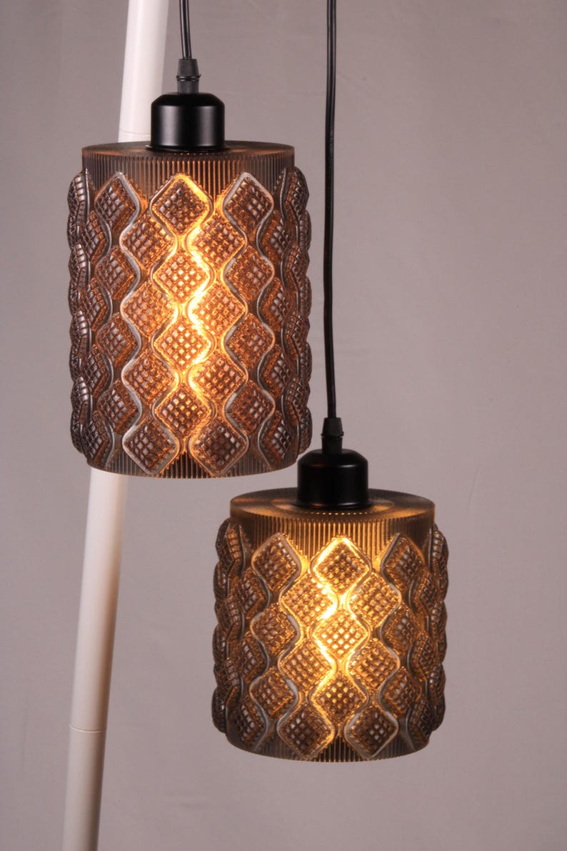 May include: Two pendant lights with a brown, textured glass shade. The shades have a diamond pattern and are lit from within, creating a warm glow. The lights hang from black cords and are attached to a white pole.