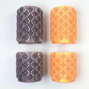 May include: Four cylindrical objects with a repeating diamond pattern. Two are a dark gray color, and two are orange. The objects are arranged in a square formation against a white background. The objects appear to be made of plastic.
