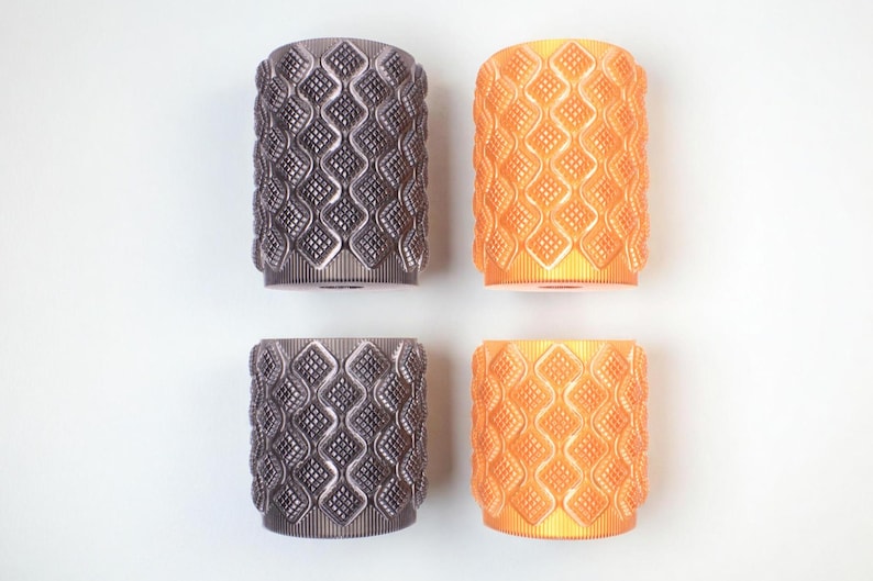 May include: Four cylindrical objects with a repeating diamond pattern. Two are a dark gray color, and two are orange. The objects are arranged in a square formation against a white background. The objects appear to be made of plastic.