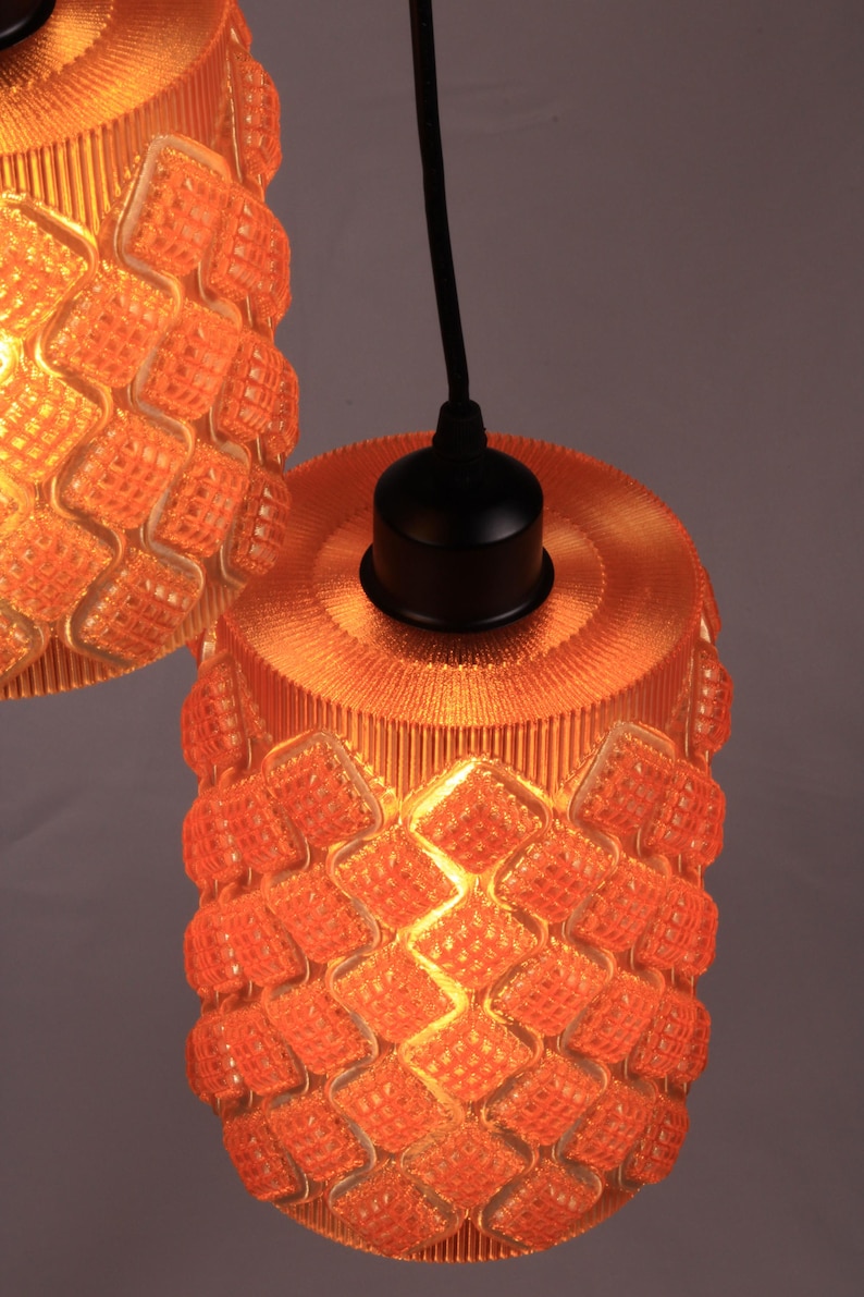 May include: Two orange pendant lights with a textured, geometric pattern. The lampshades are cylindrical with a diamond-like design. The lights hang from black cords and have black fixtures.