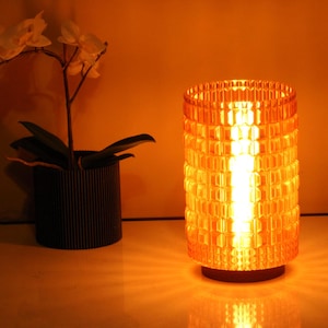 May include: A warm, amber-colored table lamp with a geometric pattern. The lamp is turned on and illuminating the surrounding area.