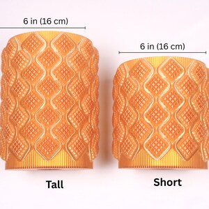 May include: Two orange decorative vases. The taller vase is 8 inches (20 cm) high and the shorter vase is 6 inches (16 cm) high. Both vases are 6 inches (16 cm) wide and have a diamond pattern.