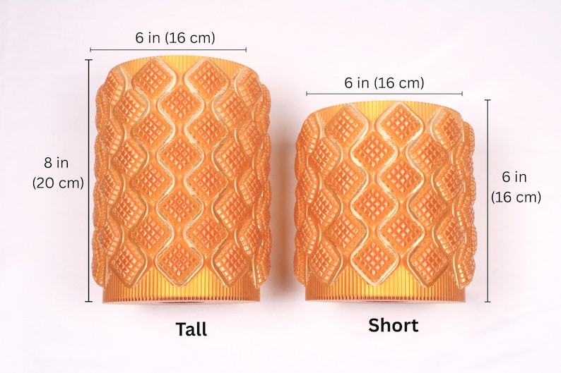 May include: Two orange decorative vases. The taller vase is 8 inches (20 cm) high and the shorter vase is 6 inches (16 cm) high. Both vases are 6 inches (16 cm) wide and have a diamond pattern.