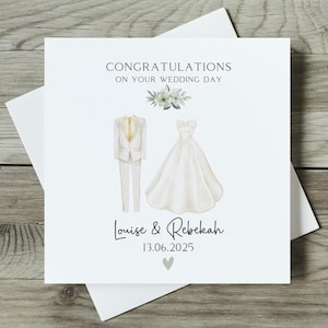 May include: A white wedding card with the text "CONGRATULATIONS ON YOUR WEDDING DAY." The card features illustrations of a suit and a wedding dress. The names "Louise & Rebekah" and the date "13.06.2025" are also printed on the card.