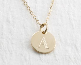 May include: A gold necklace with a small round pendant featuring the letter 'A' engraved on it.