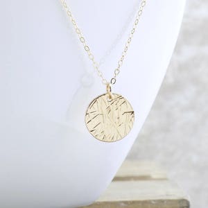 May include: A gold necklace with a textured round pendant. The pendant has a delicate, intricate design.