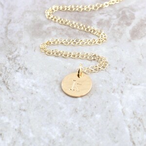 May include: A gold chain necklace with a small, round pendant featuring the letter "K" engraved on it.
