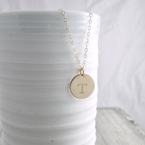 May include: A gold chain necklace with a round pendant featuring the letter "T" engraved on it.
