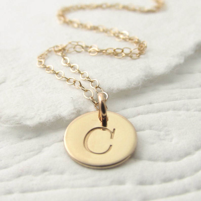 May include: A gold chain necklace with a small round pendant featuring the letter "C" engraved on it.