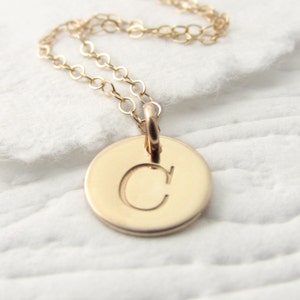 May include: A gold chain necklace with a round pendant featuring the letter "C" engraved on it.