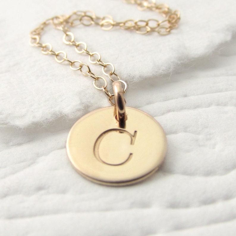 May include: A gold chain necklace with a round pendant featuring the letter "C" engraved on it.