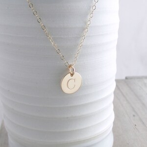 Puede incluir: Un collar de cadena de oro con un peque&ntilde;o colgante redondo con la letra "C" grabada.