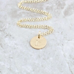 May include: A gold chain necklace with a small, round pendant featuring the letter "K" engraved on it.