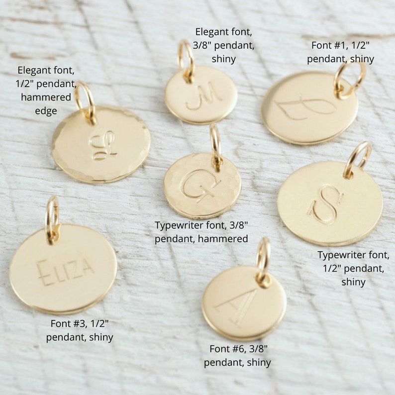 May include: Assortment of gold-toned metal pendants with different fonts and sizes. The pendants are 1/2 inch and 3/8 inch in diameter. Some pendants have a hammered finish, while others are shiny. The pendants are labeled with their font number, size, and finish.