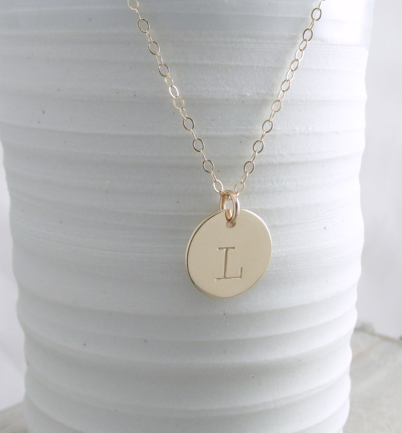 May include: A gold chain necklace with a round pendant featuring the letter "L" engraved on it.