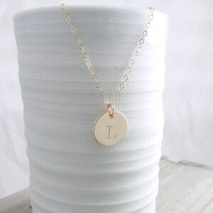 May include: A gold chain necklace with a round pendant featuring the letter "L" engraved on it.