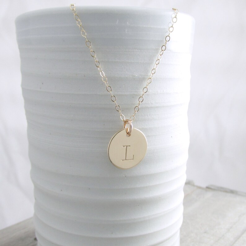 May include: A gold chain necklace with a round pendant featuring the letter "L" engraved on it.