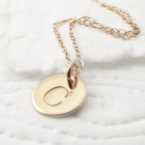 May include: A gold chain necklace with a round pendant featuring the letter "C" engraved on it.