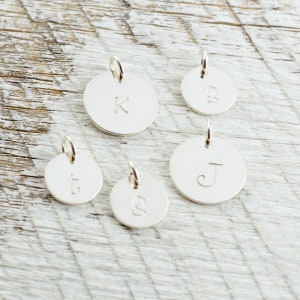 May include: Five silver charms with different letters engraved on them. The letters are K, B, t, S, and J.