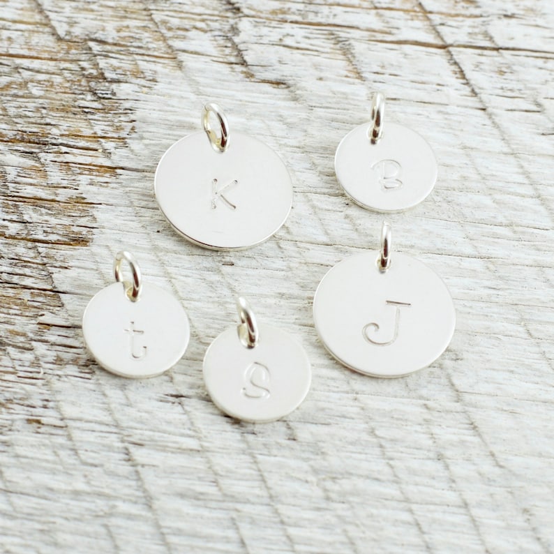 May include: Five silver charms with different letters engraved on them. The letters are K, B, t, S, and J.