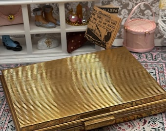 Estuche de tocador Minaudière vintage en tono dorado con marco torneado y espejo tipo peine.