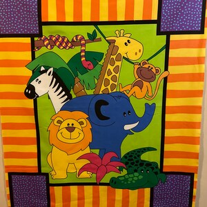 May include: A colorful fabric panel featuring cartoon animals. The design includes a zebra, lion, elephant, giraffe, monkey, and crocodile, set against a green background. The border has orange and purple stripes.