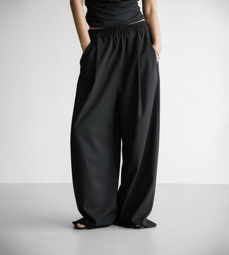 Pu&ograve; includere: Pantaloni neri a gamba larga con vita alta e coulisse. I pantaloni hanno una vestibilit&agrave; rilassata e sono realizzati in un tessuto liscio e leggero.