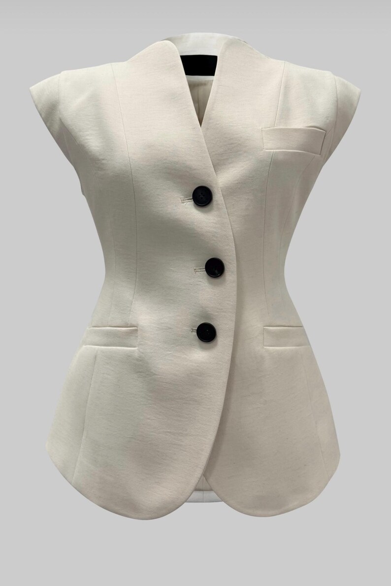 May include: Ivory-colored sleeveless vest with a tailored design. Features a V-neck, three black buttons, and two front pockets. The vest has a fitted silhouette and a classic, elegant style.